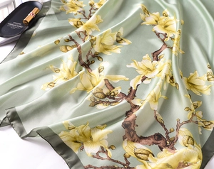 Detailed view of light green silk scarf featuring yellow magnolia print and smooth texture