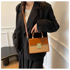 Detail of caramel leather handbag with woven texture and gold twist lock on black suit