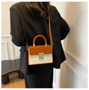 Detail of contrast color box bag with gold metal lock and leather strap on a black blazer
