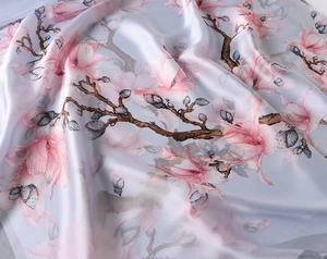 Close-up of light blue silk scarf featuring detailed pink magnolia floral patterns