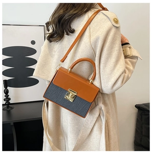 Detail view of a vintage color-block box bag with gold metal lock on a beige trench coat