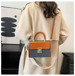 Detail of structured color-block handbag with orange flap and vertical pleats on a model