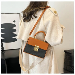 Side view of woman wearing a color-block orange and black crossbody box bag with trench coat