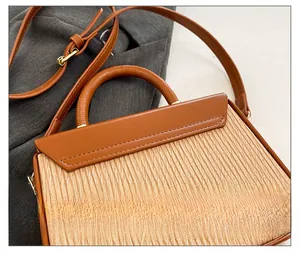 Close-up of contrast stitching, beige pleated fabric and brown leather handle on bag