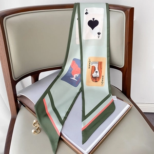 Detailansicht eines langen grünen Seidenschals mit Poker-Prints auf Ledersessel