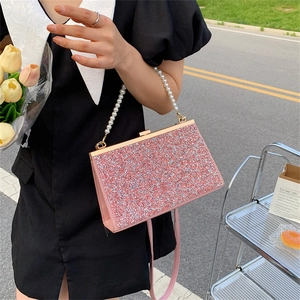 Elegant pink sequin evening bag with pearl handle and golden clasp in outdoor setting