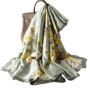 Elegant silk scarf with yellow magnolia print on light green fabric, draped over a bag