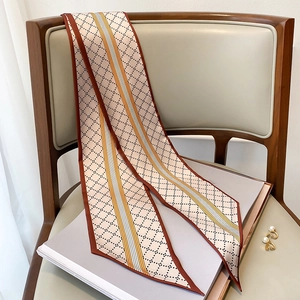 Détail d'un foulard twilly étroit à motif losanges posé sur une chaise en cuir