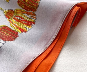 Gros plan d'un foulard carré en soie avec ourlet orange et imprimé pompons colorés