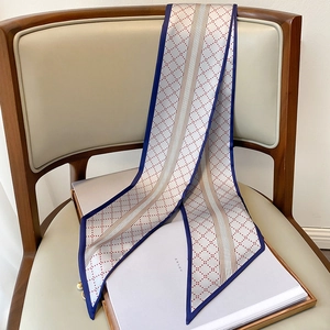 Détail d'un foulard twilly fin à pois rouges, motifs géométriques et bord bleu