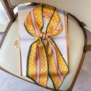 Détail d'un foulard en soie jaune avec motifs losanges noué en nœud sur un livre blanc