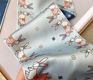 Macro detail of a light blue silk scarf featuring origami rabbit and floral prints