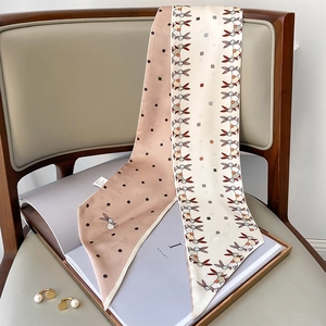 Detail of silk twilly scarf with pink rabbit patterns draped on a grey leather chair