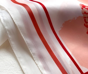 Gros plan d'un foulard carré en satin de soie montrant la texture et la bordure rouge