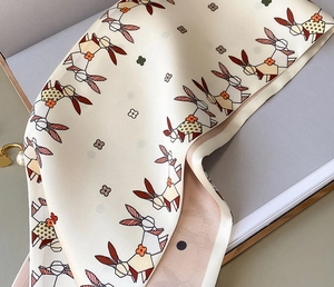Detailed macro view of beige silk-feel scarf featuring playful bunny and clover prints