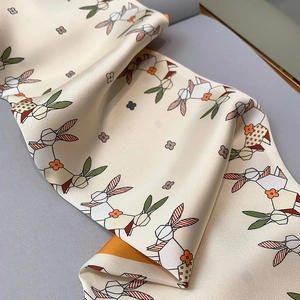 Detail of silk-like scarf with geometric rabbit pattern and vibrant orange border accents