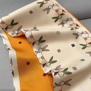Detail of silk scarf showing rabbit and floral patterns on orange and beige fabric
