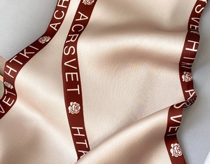 Dettaglio foulard in raso champagne con stampe floreali bordeaux e scritte eleganti