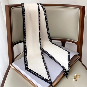 Dettaglio di un foulard sottile in seta beige con stampa di lettere su una sedia