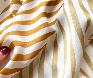 Detail shot of silky white square scarf with elegant golden wavy stripes texture