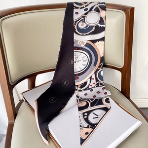 Détail d'une écharpe longue en soie avec motifs horloge et engrenages sur chaise en bois