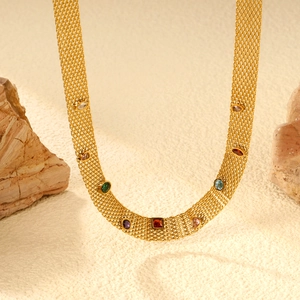Détail macro du collier en maille dorée avec cristaux colorés sur fond de pierre