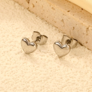 Polished silver heart stud earrings in stainless steel on a warm minimalist background
