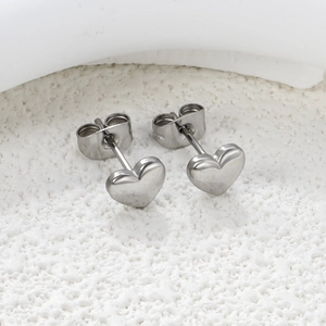 Close-up of polished silver heart stud earrings on a textured stone surface