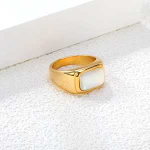 Golden signet ring featuring a rectangular white stone on a textured stone display
