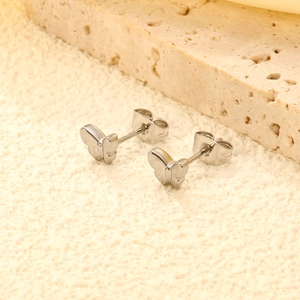 Polished silver butterfly stud earrings in stainless steel on a warm beige stone surface