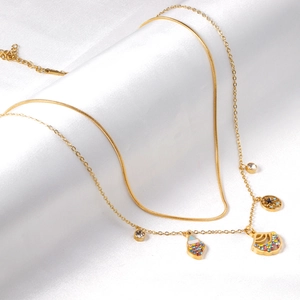 Dettaglio di una collana a strati dorata con ciondoli in strass su tessuto di seta bianca