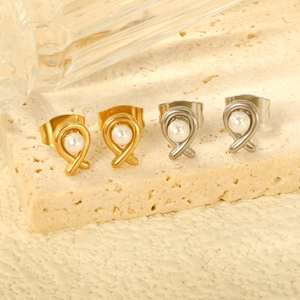 Crossed metal line pearl stud earrings in gold and silver set on a stone surface