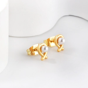Close-up of golden crossover ribbon earrings with white pearls on a white podium