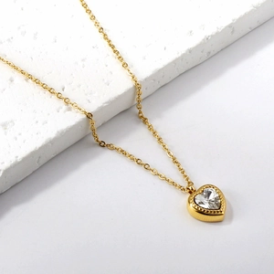 Elegant gold heart pendant necklace with clear zircon on a minimalist white stone base
