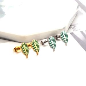 Macro detail of leaf-shaped stud earrings with gold and silver finish and green enamel inlay
