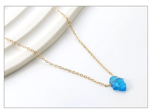 Detail of gold chain necklace with blue Hamsa Hand opal pendant on a white tray