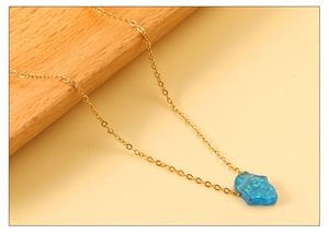 Macro detail of Hamsa Hand necklace with blue faux opal inlay and gold chain link