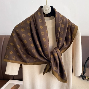 Détail d'un foulard en soie à motif monogramme marron porté sur un pull en maille beige