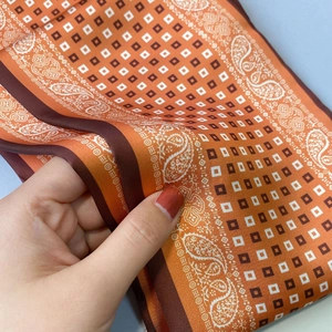 Nahaufnahme eines weichen Seidenschals mit orangefarbenem Paisley- und Geometriemuster
