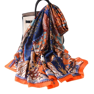 Silk satin scarf with artistic floral bird print draped over a stylish white leather handbag