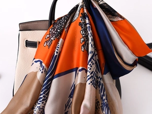 Detail of silk-feel scarf with equestrian pattern draped over a cream leather handbag