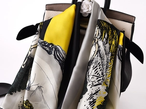 Close-up of a satin equestrian silk scarf draped elegantly over a leather handbag