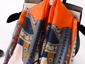 Detailed close-up of a luxury silk scarf draped on a leather handbag with floral accents