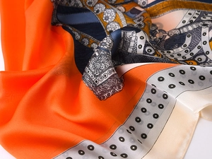 Macro detail of silk-like scarf featuring orange floral prints and geometric patterns