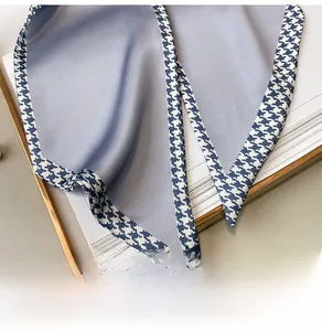 Detail of light blue satin twilly scarf with classic houndstooth edges and silky texture