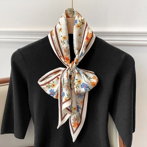Pañuelo estrecho de seda con estampado floral anudado en lazo sobre un suéter negro