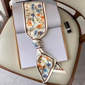 Detalle de pañuelo estrecho de seda con estampado floral anudado en una silla de madera