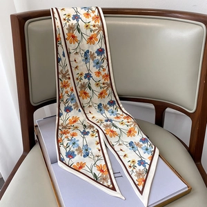 Pañuelo estrecho de seda floral sobre silla de cuero mostrando textura suave y elegante
