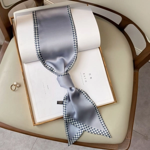 Detail of grey-blue long skinny scarf with classic houndstooth trim on a gold tray
