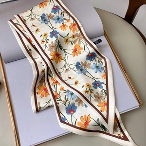 Detalle de un pañuelo de seda estrecho con estampado de margaritas y borde marrón